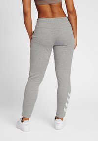 Grijze katoenen joggers van een katoenmix met een taps toelopende pasvorm, een elastische tailleband en witte chevronaccenten langs de onderkant van het been. Gecombineerd met witte sneakers.