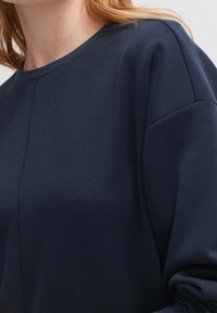 Mörkblå sweatshirt i mjuk bomull, med rund halsringning och nedhasade axlar. Enkel design utan mönster eller detaljer.