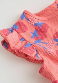 Tissu rose côtelé avec imprimés de fraises bleues et rouges et bord de manche volanté, montrant une partie d'un vêtement d'enfant.