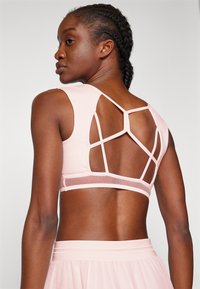 Roze sportbeha met een mesh achterkant en geometrische uitsparingen, en een gladde, aangesloten pasvorm. De stof lijkt lichtgewicht en rekbaar te zijn.