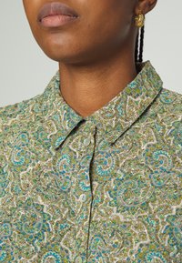 Vihreä ja sininen paisley-kuvioitu paita, jossa on kauluksellinen kaula-aukko ja napitus edessä, valmistettu kevyestä kankaasta ja sileästä tekstuurista.
