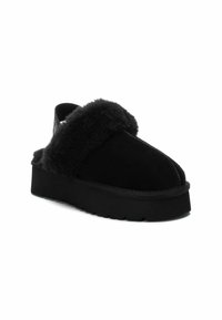Zapatos slip-on de ante negro con una banda de piel de pelo negro esponjoso, que cuentan con una suela de plataforma gruesa y un diseño de punta redondeada.