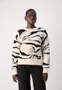 Cremfarbener Pullover mit schwarzen abstrakten Mustern, runder Halslinie und gerippten Bündchen und Saum. Der Stoff wirkt weich und strukturiert.