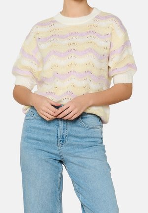 Person iført lyseblå jeans og en kortærmet striktrøje med pastelfarvede gule, lyserøde og hvide bølgede striber.