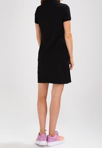 Abito polo nero con maniche corte, dalla forma leggermente aderente e design sobrio, abbinato a sneakers rosa e bianche.