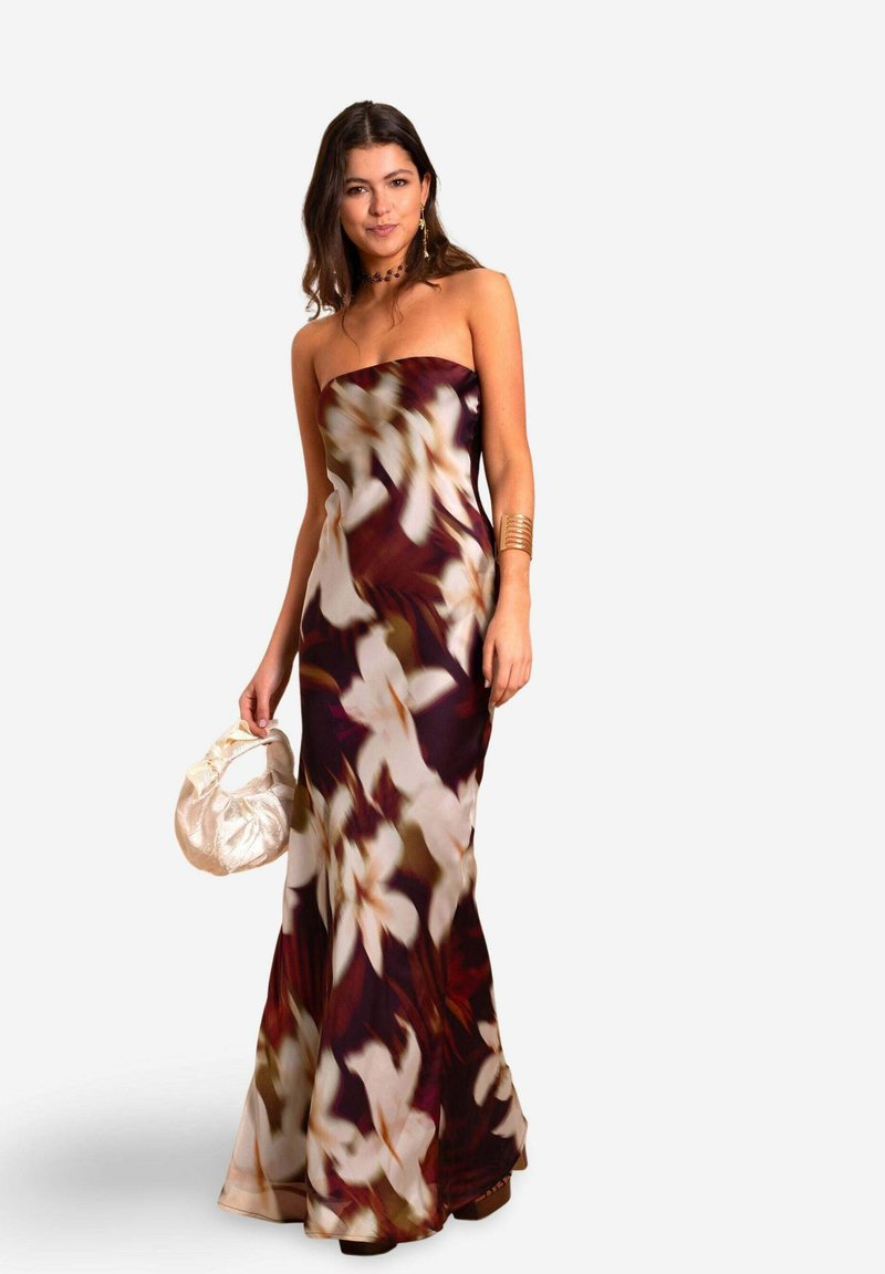 Trägerloses Maxikleid mit floralem Muster, das eine Mischung aus weißen und burgunderfarbenen Blüten auf einem fließenden Stoff zeigt. Kombiniert mit einer Seiden-Clutch und goldenen Accessoires.