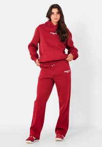 Rode hoodie en joggingbroek set, gemaakt van zachte stof. De hoodie heeft een voorzak en logo, de broek heeft een koord en logo aan de zijkant.