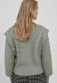 Gestrickter Pullover in sanftem Grün mit strukturierten Zopfmustern und Rippstrickmustern, breiten Schultern und einem lässigen Schnitt. Weiche, voluminöse Wolle.