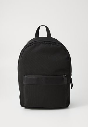 Black fabric backpack with a rounded shape, featuring a front zippered pocket and a top handle for carrying. Smooth texture and minimalist design.