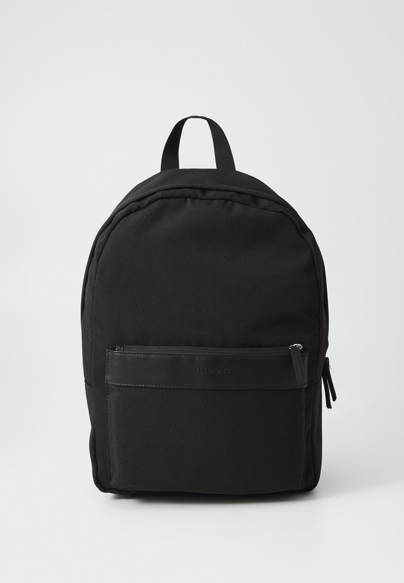 Svart stoffryggsekk med rund form, med en frontlomme med glidelås og et håndtak på toppen for bæring. Glatt tekstur og minimalistisk design.