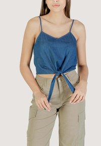Top corto in denim blu scuro, con spalline sottili e un dettaglio di nodo nella parte anteriore. Abbinato a pantaloni cargo color khaki chiaro. Texture liscia.