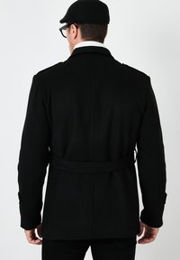 Abrigo de mezcla de lana negra con cinturón en la cintura, cuello puntiagudo, hombreras y puños abotonados. Textura suave con un diseño clásico.
