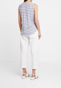 Top sin mangas a rayas en azul y blanco, con pliegues en la parte trasera. Combinado con pantalones blancos de corte suelto y sandalias claras.