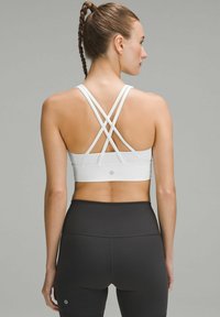 White sports bra with crossback straps, smooth texture, and logo on the back, paired with black leggings featuring a snug fit and seam details.
