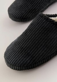 Black corduroy slippers with a smooth, plush interior, rounded toe design, and ribbed texture on the exterior for grip.