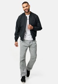 Veste bomber noire, t-shirt blanc, pantalon gris clair et baskets noires. La veste présente une fermeture éclair et des poches latérales.