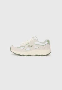 Des baskets athlétiques en crème clair avec des accents verts, comprenant des matériaux en maille et en daim, un bout arrondi et une semelle en caoutchouc texturée.