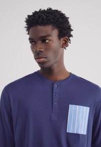 Marineblauwe longsleeve shirt van een gestructureerde ribstof, met een contrasterende lichtblauwe gestreepte zak en een henley-halslijn met vijf knopen.
