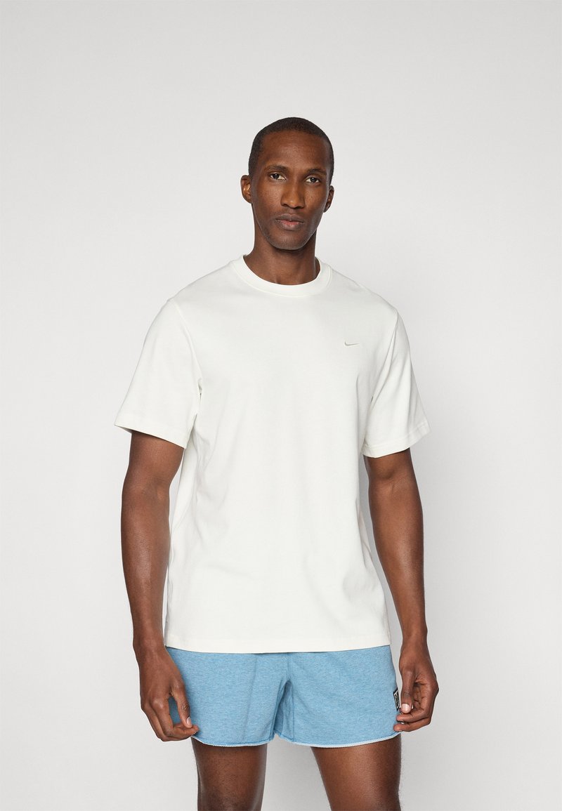 Camiseta blanca de manga corta con cuello redondo y un pequeño detalle de logo en el pecho, combinada con pantalones cortos de color azul claro.