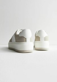 Zapatillas de plataforma beige y blancas, con un upper de cuero suave y paneles de ante texturizados, puntera redondeada y suela de goma con agarre.