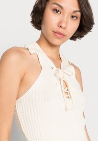 Top de malha canelada em marfim com decote halter, detalhe frontal com atacadores e tecido texturizado. Realçado com um colarinho suave.