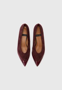 Escarpins bordeaux à bout pointu, présentant un mélange de cuir lisse et de daim, avec une découpe basse et un design minimaliste. La semelle intérieure est beige.