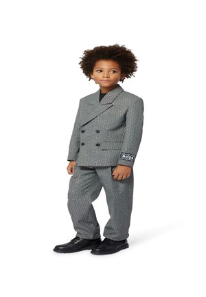 Costume gris croisé avec une texture à motifs, avec des boutons noirs et un patch logo "BOSS" sur la manche, associé à des chaussures noires.