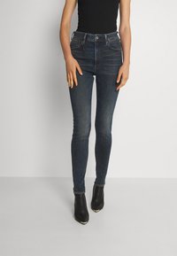 Mörkblå skinny jeans i denim med en urtvättad yta, med fem fickor och dragkedja, kombinerat med svarta ankboots.