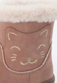 Bota de tela rosa con forro de piel sintética y un diseño de cara de gato, con bordado dorado y un acabado texturizado en la parte superior.