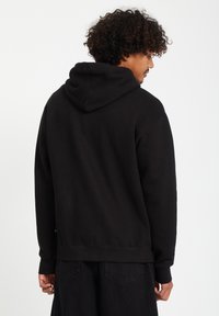 Black hoodie featuring a kangaroo pocket, ribbed cuffs, and a drawstring hood. Soft fabric with a relaxed fit, worn with dark pants.