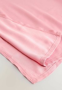 Vaalea va fabric, sileä tekstuuri, taitettuna esitellen helman ja ompeluyksityiskohdat. Yksinkertainen, koristelematon muotoilu puhtaalla, tasaisella viimeistelyllä.
