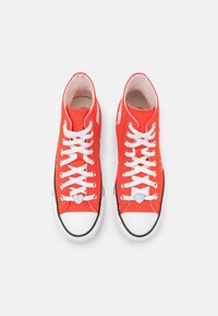 High-top sneakers in bright red canvas with white laces, black rubber soles, and heart-shaped lace charms, featuring a rounded toe design.