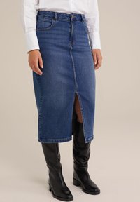 Fustă tip creion din denim bleu închis, cu o fante pe față, talie medie și design cu cinci buzunare, combinată cu cizme din piele neagră până la genunchi.