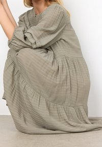 Groene, gestructureerde, lange mouw jurk met een vloeiende ontwerp en gathered lagen. Heeft een ronde halslijn en geplooide accenten.