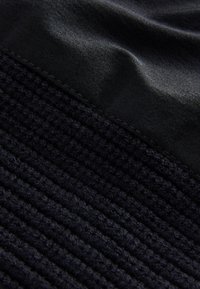 Mustast kangast, millel on tekstuuriga punutud muster, kõrval sile kangas, mõlemad erinevates musta toonides. Õmblused on korralikult viimistletud.