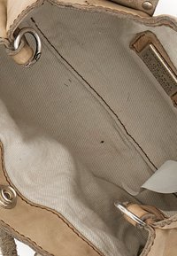 Interno di borsa in pelle beige con una texture morbida, rivestito in tessuto a righe. Include elementi metallici e una piccola etichetta.