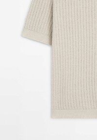 Light beige knitted top with short sleeves, featuring a textured pattern and ribbed hem. Made of a soft, breathable material.
