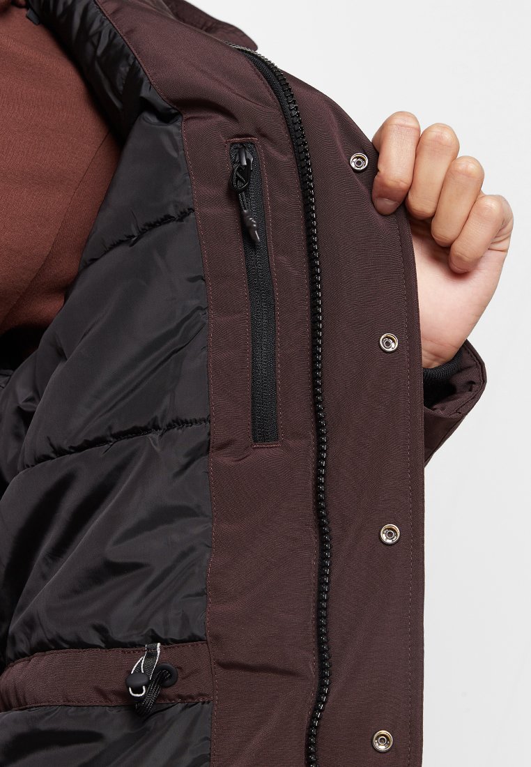 Donkerbruin pufferjack-interieur met contrasterende zwarte voering, voorzien van een ritszak, drukknoopsluitingen en een verstelbaar aantrekkoord.