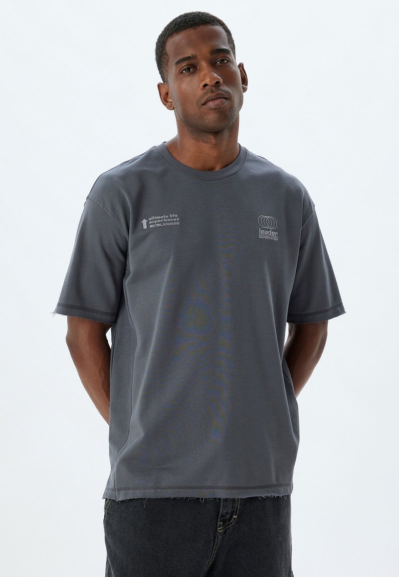 Grå bomulds t-shirt med korte ærmer, ribbet halsudskæring og slidset kant. Har hvide tekst- og logoaccentuer på forsiden.