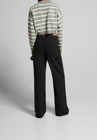 Top court avec des rayures grises et blanches, associé à un pantalon noir ample avec poches et une silhouette décontractée.