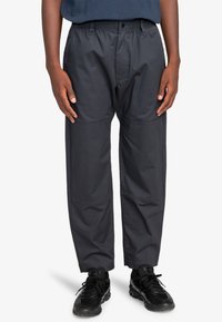 Donkergrijze lichtgewicht broek met een relaxte pasvorm, voorzien van een elastische tailleband en zichtbare kniestukaccenten. Gepaard met zwarte sneakers.