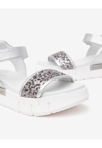 Sandales argentées avec des accents en sequins, une large bride sur le bout, des brides réglables à la cheville et une semelle épaisse blanche.