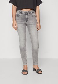Grå skinny jeans med falmet finish, klassisk fem-lommers design og lynlås. Brukt med svarte hælhæler.
