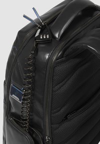 Zaino in pelle nera con texture imbottita, molteplici cerniere, una serratura a combinazione di sicurezza e un laccio avvolto per maggiore protezione.