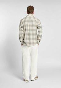 Camicia a quadri in toni tenui di beige e azzurro chiaro, con maniche lunghe, polsini con bottone e una vestibilità comoda, abbinata a pantaloni bianchi e scarpe casual.