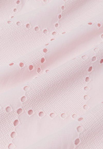 Tessuto rosa chiaro con un motivo a griglia testurizzata e fori ricamati, che creano un bordo scalloppato lungo un lato.