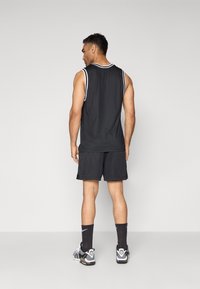 Svart atletisk tanktopp med hvite detaljer, kombinert med svarte mesh-shorts. Antrekket har sportige designfunksjoner og pustende stoff.
