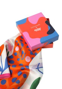 Svilena ruta v živo oranžni, modri in roza barvi z abstraktnimi vzorci, razstavljena ob roza škatli z barvitimi oblikami in besedilom blagovne znamke.