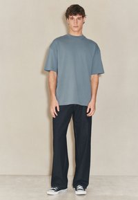 Tricou cu mânecă scurtă, albastru deschis, asortat cu blugi din denim închis. Blugii au croială dreaptă, iar ținuta este completată de adidași negri.