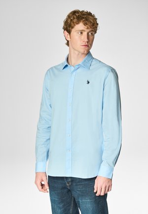 Camicia a maniche lunghe di colore azzurro chiaro realizzata in tessuto morbido, con chiusura a bottoni sul davanti e un piccolo logo scuro sul lato sinistro del petto.